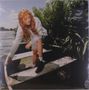 Ein Mädchen mit langen, lockigen Haaren sitzt in einem Boot und blickt nach unten; im Hintergrund Wasser und Pflanzen., LP