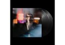 Unschärfe eines Mannes mit Brille, hellem Pullover, Neonlichter spiegeln sich. Dahinter schwarze Schallplatten., 1 CD und 1 LP