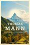 "THE MAGIC MOUNTAIN, THOMAS MANN, TRANSLATED BY SUSAN BERNOFSKY" vor einer Berglandschaft mit blauem Himmel und Wäldern., Buch