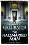 Text: "Robert Galbraith, The Number One Bestseller, The Hallmarked Man, A Strike Novel."  
Zwei Personen betreten ein beleuchtetes Gebäude., Buch