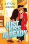 In großen Buchstaben steht "JUST KISS ALREADY". Ein Paar in moderner Kleidung steht sich nah in einer Bibliothek., Buch
