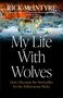 „My Life With Wolves“ von Rick McIntyre. Ein Wolf steht im Schnee vor einem warmen, bewaldeten Hintergrund., Buch