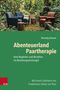 "Abenteuerland Paartherapie" von Hartwig Hansen. Zwei Stühle im Wald, Tische aus Baumstümpfen, Tuch auf einem Stuhl., Buch