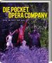 Titel: "DIE POCKET OPERA COMPANY". Untertitel: "OPER AM PULS DER ZEIT". Szene: Personen im Kostüm in einem Wald, beleuchtet., Buch