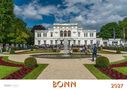 Text: "BONN 2027". Eine große weiße Villa, umgeben von einem gepflegten Garten mit Springbrunnen und Menschen., Buch