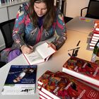 Eine Frau signiert ein Buch mit dem Titel "Judith Holofernes – Die Träume Anderer Leute" an einem Tisch.