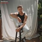 Text: "Niall Horan Dinner Party". Ein Mann in schwarzem Tanktop und weißer Hose sitzt auf einem Hocker vor einem hellen Vorhang.