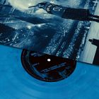 Ein Plattencover zeigt einen Künstler auf einer Bühne mit einem Mikrofon. Eine blaue Vinylplatte mit Titelliste ist sichtbar.
