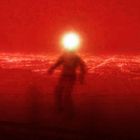 Eine Silhouette vor rotem Hintergrund, mit einem hell leuchtenden Kopf, in einer verschwommenen Lichterlandschaft.
