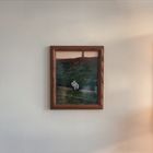 Ein gerahmtes Foto zeigt eine Person, die an einem grasbewachsenen Hang sitzt. Im Hintergrund steht ein Baum.