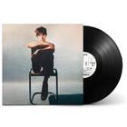 Ein Mann sitzt nachdenklich auf einem Stuhl. Vor ihm ist eine schwarze Vinyl-Schallplatte zu sehen.