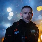 Ein Polizist in Uniform mit dem Wort "POLICE" im Brustbereich, umgeben von Funken und verschwommenen Lichtern.