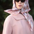 Es gibt keinen sichtbaren Text. Eine Person mit Sonnenbrille und Kopftuch trägt einen hellrosa Mantel.