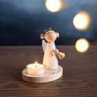 Ein Engel aus Holz mit Heiligenschein und glühendem Teelicht auf einem Tisch, vor einem dunkelblauen Hintergrund.