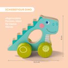 „SCHIEBEFIGUR DINO“; „abgerundete Formen, ideal für kleine Hände“. Illustration eines blauen Dino-Spielzeugs auf Rädern.