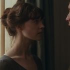 Eine Frau und ein Mann stehen sich nah vor einem Fenster gegenüber, beide in historischer Kleidung, ernsthaft blickend.