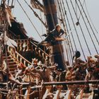 Ein belebtes Piratenschiff-Deck mit kämpfenden Figuren, ein Mann hängt am Mast, andere Figuren sind in Aktion vertieft.