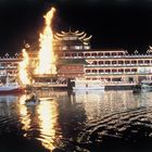 "The Floating Dragon Restaurant" brennt kräftig auf einem beleuchteten Boot mit geschwungenen Dächern auf dunklem Wasser.