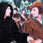 Zwei Männer in mittelalterlicher Kleidung, einer trägt braunes Leder und einen Bogen, der andere eine schwarze Kutte mit Kapuze.