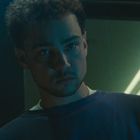 Ein nachdenklicher junger Mann in bläulichem Licht in einem dunklen Raum.