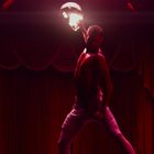 Ein Mann hebt innen einen brennenden Football-Helm hoch. Im Hintergrund sind rote Vorhänge und Football-Trikots.