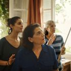 Drei Frauen stehen in einem lichtdurchfluteten Raum und blicken nach oben, umgeben von Pflanzen am Fenster.