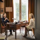 Zwei Frauen sitzen sich in einem Büro mit einem Schreibtisch gegenüber. Eine schreibt, die andere hört zu. Im Hintergrund ein Fenster.