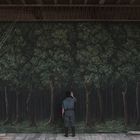 Ein Mann steht vor einer großen, detaillierten Waldgemälde-Kulisse auf einer Holzbühne.