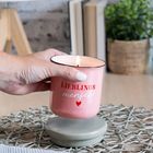 Text "LIEBLINGS mensch" auf rosa Kerze. Eine Hand hält sie, Tisch mit Büchern und Pflanze im Hintergrund.
