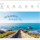 MÄRZ, KW 10: 8-14. Ein Steinweg führt zu einem blauen Meer mit Felsen, umrahmt von Pflanzen.