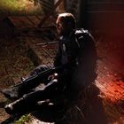 Ein Mann in Polizei-Uniform sitzt mit einem Gewehr auf dem Boden. Er wirkt erschöpft und ist von rotem Licht beleuchtet.