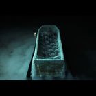 Ein heller, spitz zulaufender Kegel auf dunklem Hintergrund, bedeckt mit transparentem Stoff, daneben eine kleine Kerze.