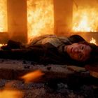 Ein Mann liegt auf einem Boden voller Schutt, umgeben von einem brennenden Feuer.