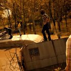 Eine Gruppe von vier Personen steht auf einem halb versunkenen Wohnmobil in einem überfluteten Waldgebiet.