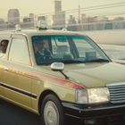 Taxi-Aufschrift auf einem gelben Taxi mit Fahrgästen; Stadtansicht im Hintergrund bei Sonnenuntergang.