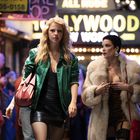 Leuchtreklame mit Text "ALL NUDE HOLLYWOOD NEW WORLD" vor einer belebten Straße bei Nacht mit zwei Frauen im Vordergrund.