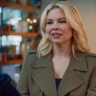 Zwei Frauen sitzen in einem Café. Eine hat blondes, schulterlanges Haar und trägt einen grünen Mantel.