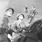 Zwei Personen in Uniformen bedienen eine große Maschine, umgeben von Rauch. Sie blicken entschlossen in die Ferne.