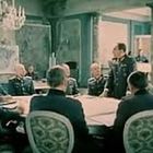 Ein Raum mit Männern in Militäruniformen, die um einen Tisch sitzen. Einer steht und scheint eine Rede zu halten. Elegantes Dekor.