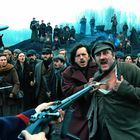 Eine Menschenmenge konfrontiert einen Soldaten mit einer Schusswaffe. Die Szenerie wirkt dramatisch und angespannt.