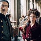 Zwei Personen in historischer Kleidung in einem Säulengang; eine Frau mit aufwendiger Frisur und ein Mann mit ernstem Blick.