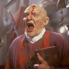 Ich kann den Text auf dem Buch nicht lesen. Ein Mann mit maskenhaftem Gesicht schreit, Blut fließt über seine Stirn.