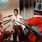 FSK ab 12 freigegeben. Ein Mann in weißem Hemd wird von mehreren Personen mit Lanzen umringt. Sie tragen rote Uniformen.