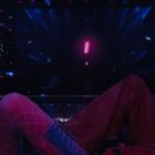 Zwei Frauen in einem dunklen Raum mit bunten Lichtern und Glitzerkleidung, eine trinkt aus einem Glas.