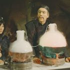 "FU-M" steht rechts auf einer Tafel. Zwei Personen in asiatischer Kleidung, vor dampfenden Glasgefäßen in einem Labor.