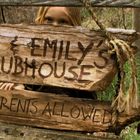 "Jack & Emily's Clubhouse. No Parents Allowed." Ein Mädchen schaut neugierig durch einen Holzzaun.