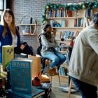 Bücher mit Titeln "The Last Days of Santa Claus" und "Elves Unite". Weihnachtlich dekorierter Raum mit Menschen.