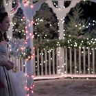 Keine Texte. Eine Frau im Abendkleid und ein Mann im Anzug stehen sich auf einer weihnachtlich beleuchteten Veranda gegenüber.