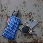 Schwarze Brille in blauem Etui mit Muster. Daneben ein Smartphone und ein Schlüsselbund auf rostigem Hintergrund.