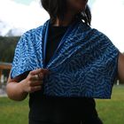 Eine Frau trägt ein blau-weiß gemustertes Tuch. Ihre Hand hält das Tuch über einem schwarzen Oberteil. Im Hintergrund ist Natur.